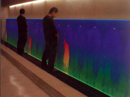 Two men urinating on a urinal wall that changes color from blue/green to red/orange when activated
